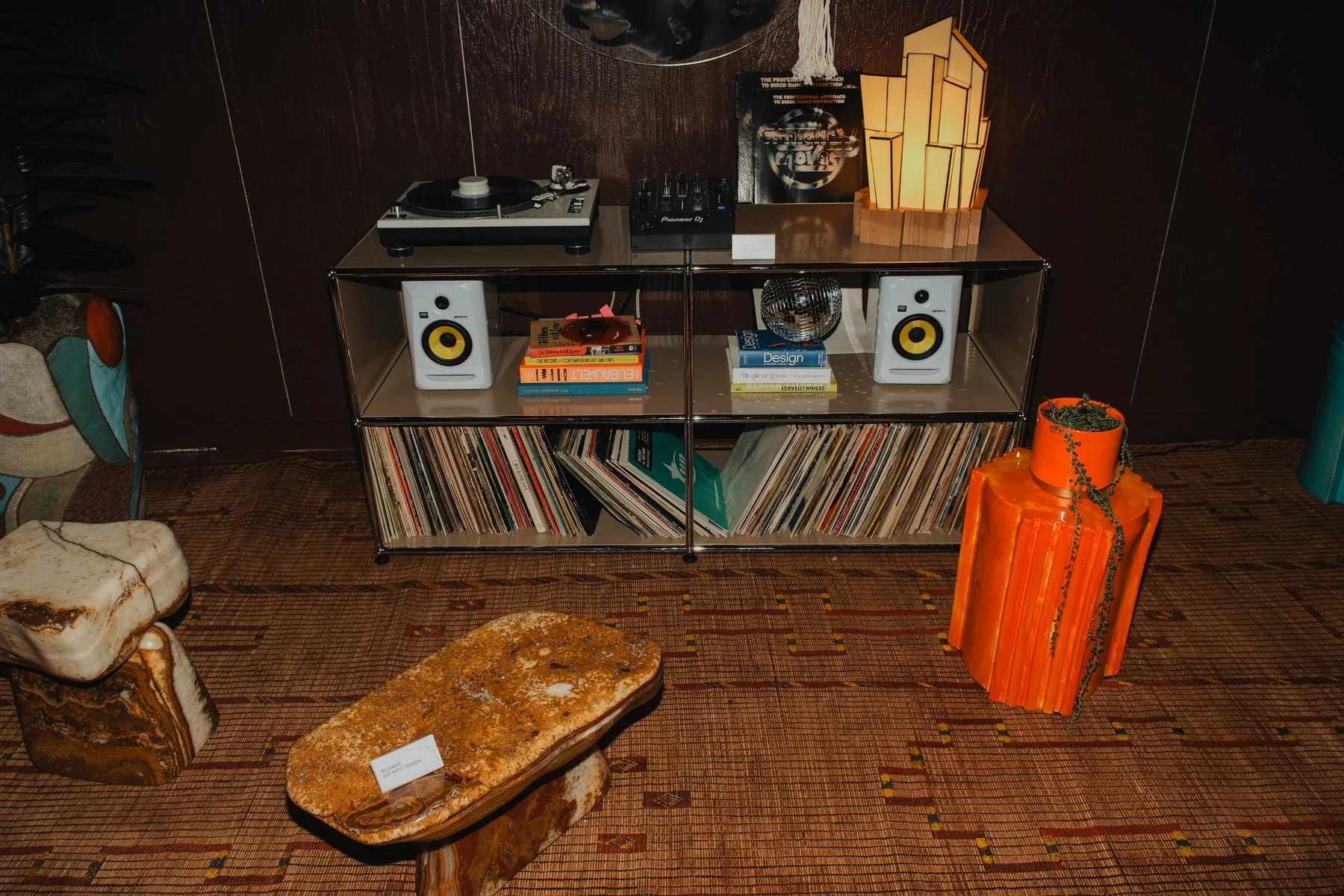 Turntable, mixer and a shelf of disco records with stone stools in front