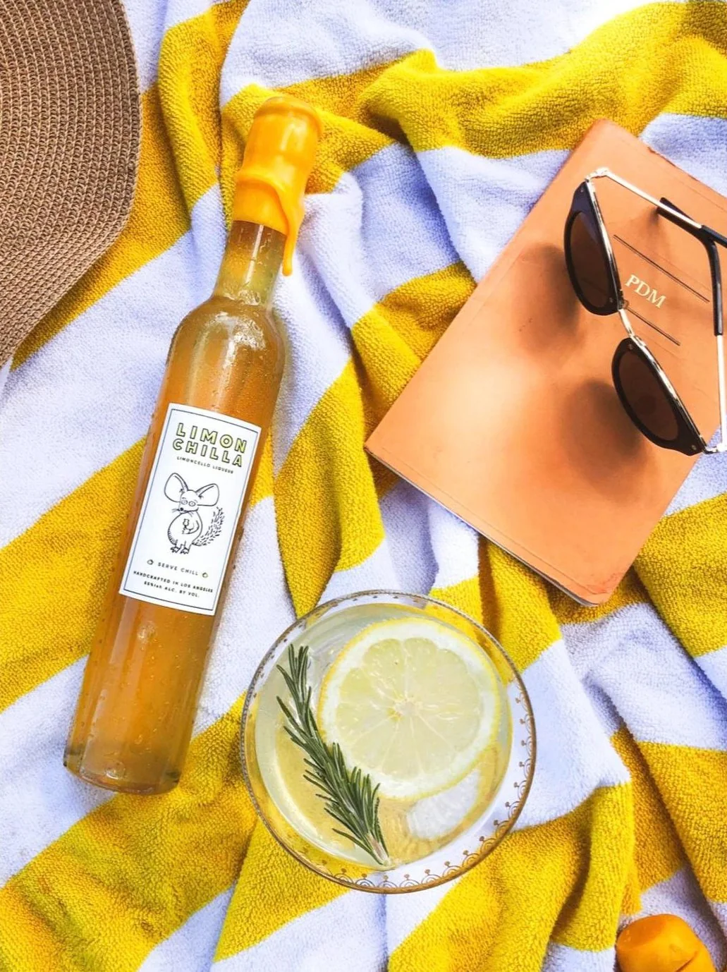 A bottle of Limonchilla and a glass with lemon and rosemary on a striped beach towel