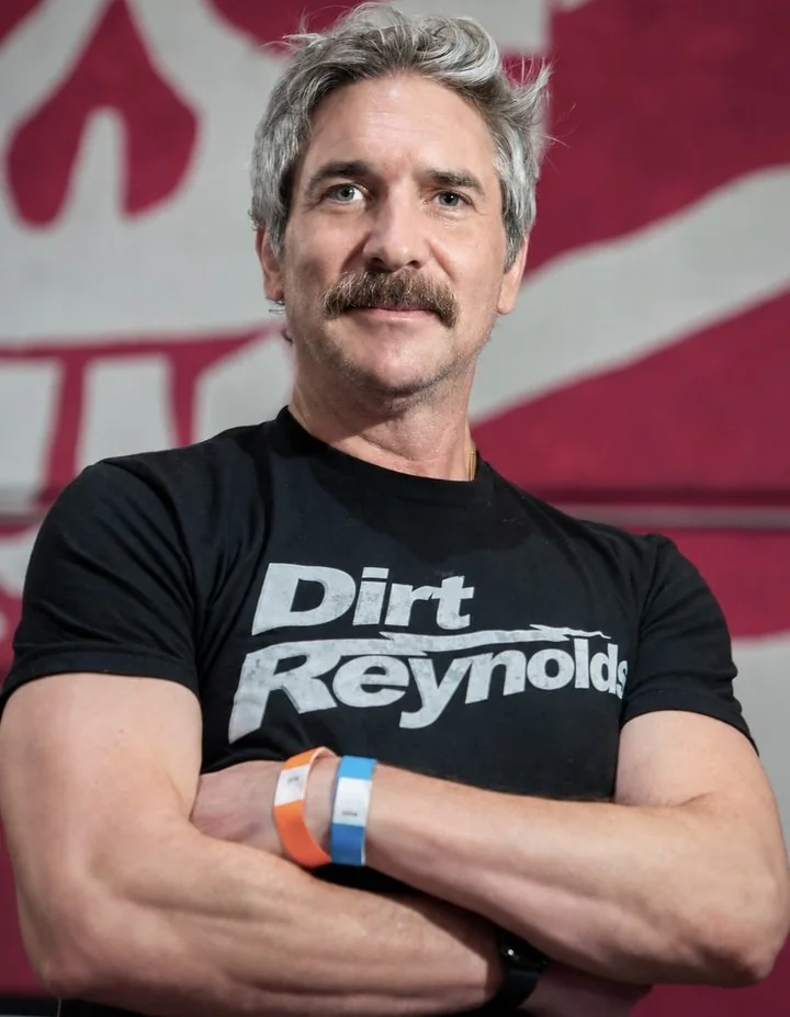 Peter Megler, arms crossed, in a Dirt Reynolds T-shirt in front of a red mural